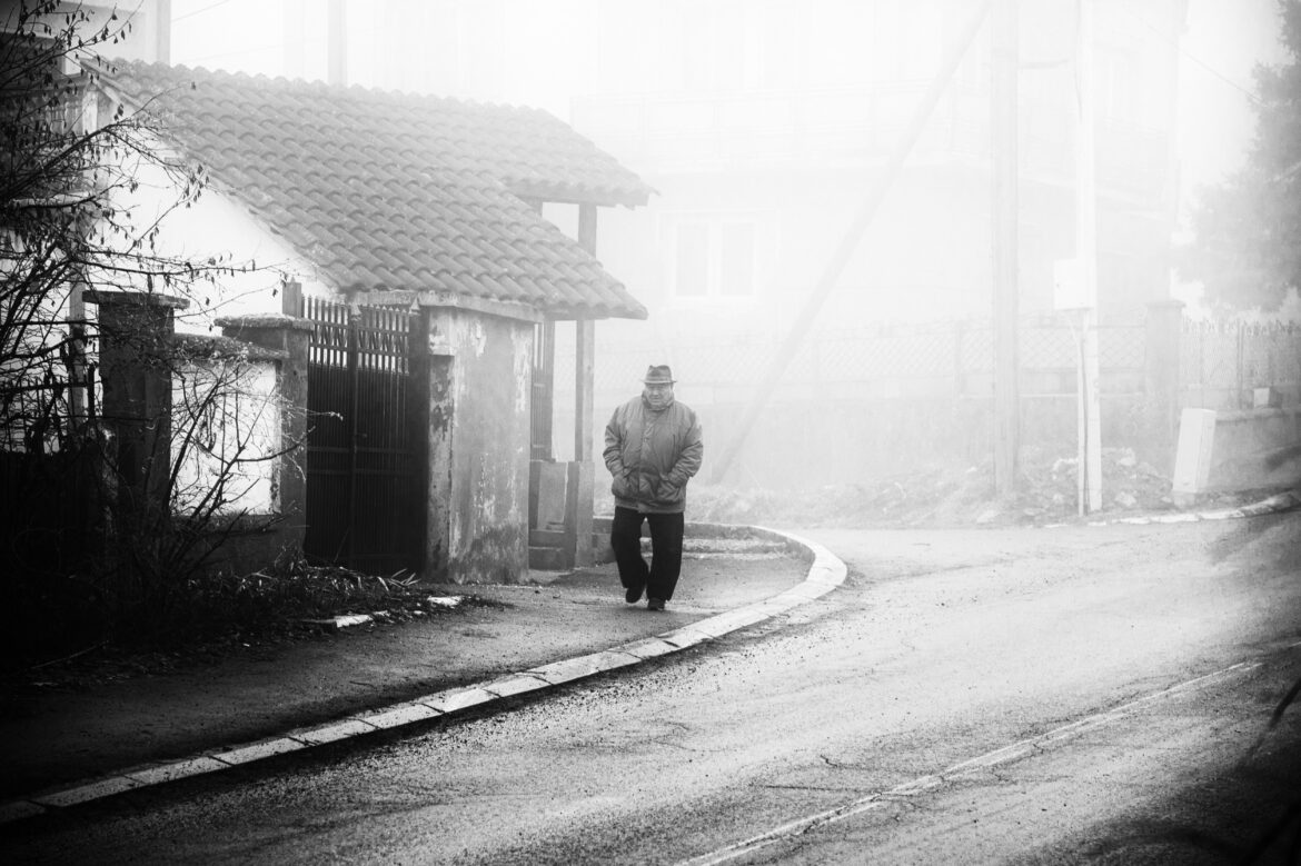 A man walking through a foggy street in a quiet neighbourhood, evoking a sense of nostalgia and solitude.